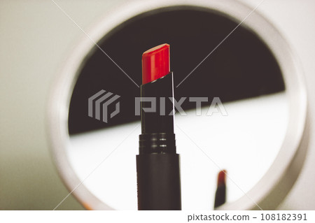 Classic women's makeup. Red lipstick in a black tube next to a round mirror on a makeup table. Cosmetic concept contrast grey white background. Decorative cosmetics sample. Reflection of lipstick. 108182391