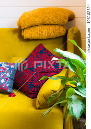 Home modern interior design detail. Vertical photo with mustard yellow sofa and warm wool plaid, soft decorative bright pillows and potted green flower indoors. Apartment living room cozy decor. 108182564
