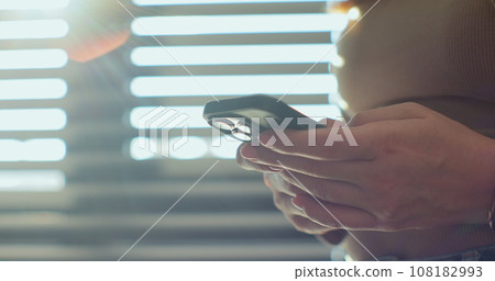 Side view. Hand of woman using smartphone at home. Close up of female hands texting on smartphone. Side view. Hand of woman using smartphone at home. Close up of female hands texting on smartphone. 108182993
