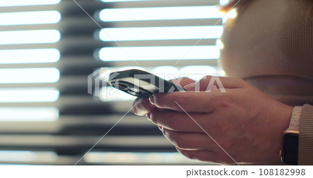 Hand of woman using texting mobile phone or chat. Close up of woman hand. Sunlight. Hand of woman using texting mobile phone or chat. Close up of woman hand. Sunlight. 108182998