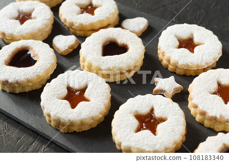 Homemade Linzer cookies sprinkled with powdered sugar with apricot jam on a black background. Festive tasty treats. 108183340