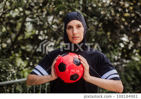 Beautiful female football player in hijab with ball in her hand. The woman plays soccer for relaxation. Concept of muslim woman in sport. 108184981