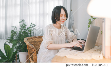 Asian woman using laptop computer at living home apartment cozy room style with plant wood table 108185002