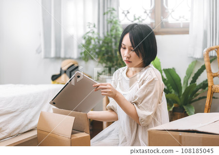 Asian woman unpack parcel box for new laptop in cozy bedroom Asian woman unpack parcel box for new laptop in cozy bedroom 108185045