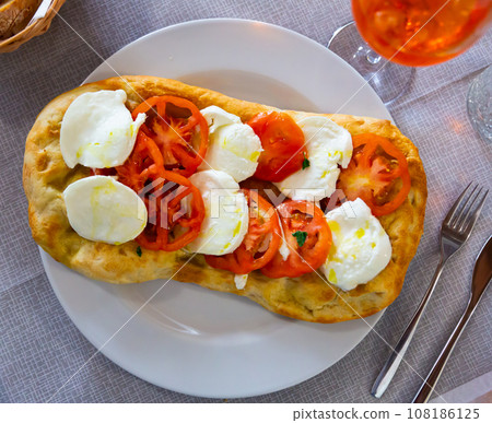 Pizza pinsa with sliced buffalo mozzarella and beef heart tomatoes Pizza pinsa with sliced buffalo mozzarella and beef heart tomatoes 108186125
