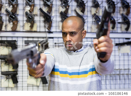 Hispanic man aiming with two pistols in armory shop 108186146