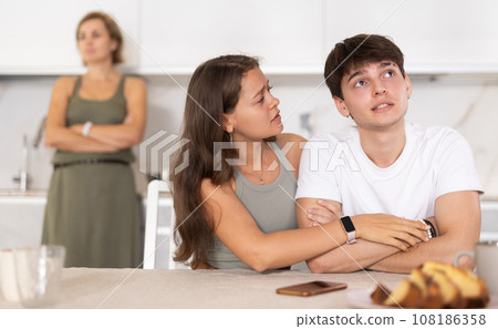 Frustrated guy sits near kitchen table and worries about quarrel with his mother. 108186358