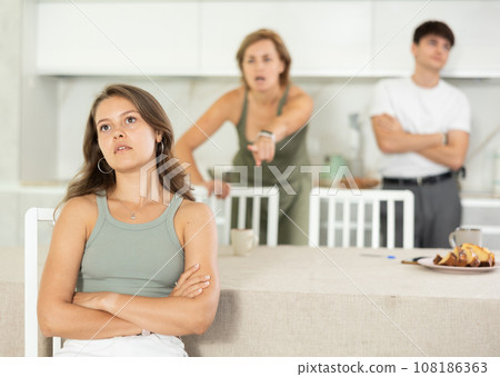 Mother-in-law and son scold young daughter-in-law in home kitchen 108186363