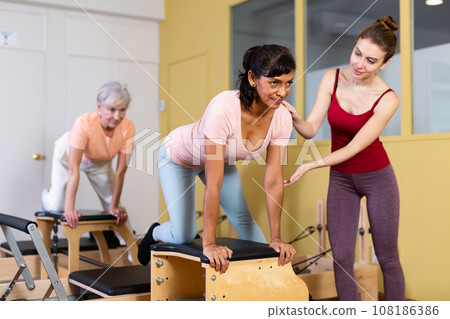 Hispanic woman doing pilates on combo chair with personal trainer 108186386