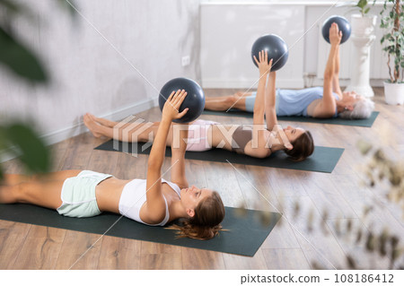 Teenage girl doing pilates with soft ball in group Teenage girl doing pilates with soft ball in group 108186412