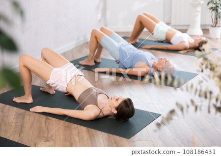 Mom, grandma and teen daughter do half bridge Setu Bandha Sarvangasana, glute bridge pose 108186431