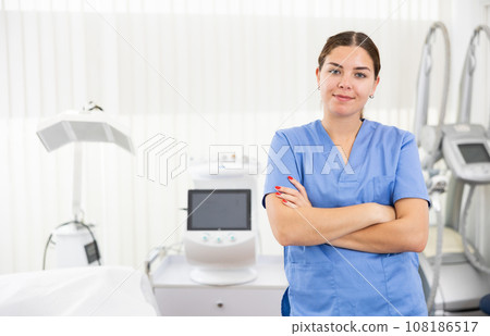 Young woman cosmetologist standing with crossed hands, smiling and looking at camera in clinic of aesthetic medicine Young woman cosmetologist standing with crossed hands, smiling and looking at camera in clinic of aesthetic medicine 108186517