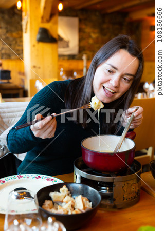 Young adult woman eating fondue at restaurant 108186666