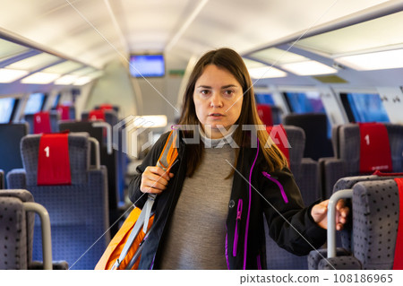 Woman with backpack on shoulder standing in aisle between seats in train Woman with backpack on shoulder standing in aisle between seats in train 108186965