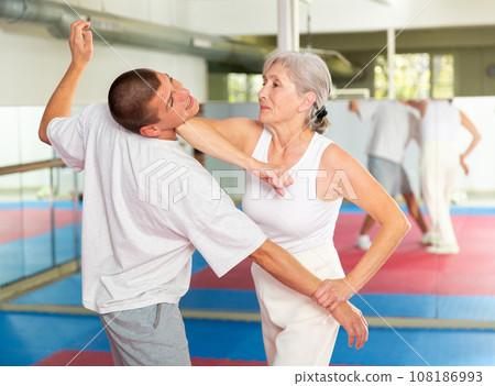 Elderly woman performing elbow strike and wristlock to man in self defense training 108186993