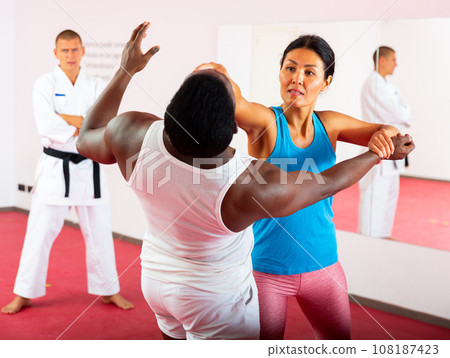 Woman exercising self-defence moves, trainer watching them 108187423