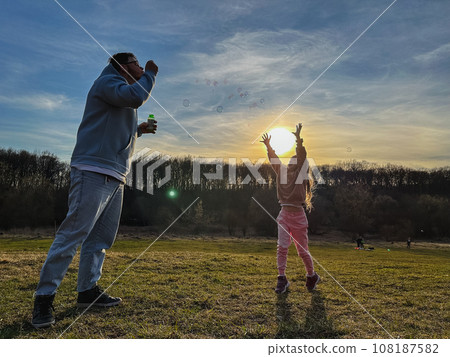 happy man with little girl playing with soap bubbles happy man with little girl playing with soap bubbles 108187582