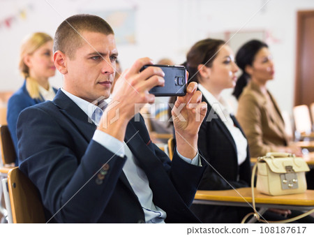 Man recording lecture on smartphone at conference Man recording lecture on smartphone at conference 108187617