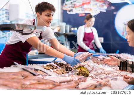 Portrait of man offering fresh fish striped red mullet at seafood shop 108187696