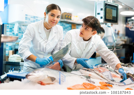 Proficient sellers cutting piece of tuna on tabletop in fish store 108187843