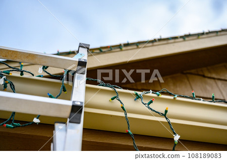extension step ladder against side of roof with a strand of Christmas lights 108189083