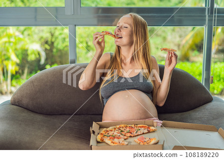A pregnant woman enjoys a slice of pizza, savoring a moment of indulgence while satisfying her craving for a delightful, comforting treat. Excited Pregnant Young Lady Enjoying Pizza Holding Biting 108189220