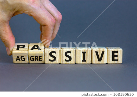Hand turns cubes and changes the word 'passive' to 'aggressive', or vice versa. Business and psychological concept. Beautiful grey background, copy space. Hand turns cubes and changes the word 'passive' to 'aggressive', or vice versa. Business and psychological concept. Beautiful grey background, copy space. 108190630
