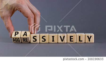 Passively or aggressively symbol. Businessman turns cubes and changes the word passively to aggressively. Psychological and passively or aggressively concept. Beautiful grey background, copy space. Passively or aggressively symbol. Businessman turns cubes and changes the word passively to aggressively. Psychological and passively or aggressively concept. Beautiful grey background, copy space. 108190633