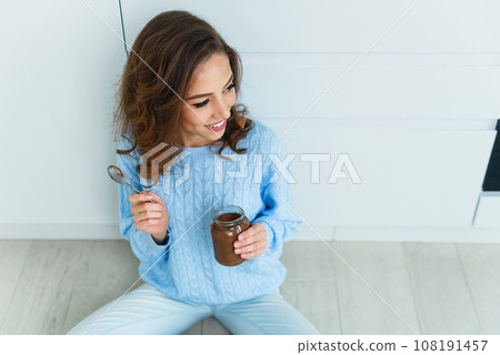 Pretty exuberant young woman in modern stylish clothes enjoying tasty chocolate and looking at camera with cute smile in the cuisine interier Pretty exuberant young woman in modern stylish clothes enjoying tasty chocolate and looking at camera with cute smile in the cuisine interier 108191457