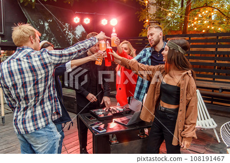 Cheerful friends having fun on birthday party celebration and clinking bottles with colourful beverages during energy party in garden house. Weekend, summer nights and people concept. 108191467