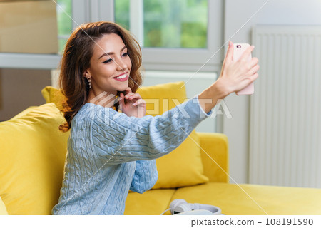 Beautiful girl with cute smile makes selfie on the cuisine background. Cheerful girl speaks online with her boyfriend by smartphone. Beautiful girl with cute smile makes selfie on the cuisine background. Cheerful girl speaks online with her boyfriend by smartphone. 108191590