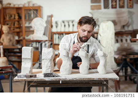 Stonemason which sitting in creative workshop and scraping the remains of lime-stone using brush 108191731