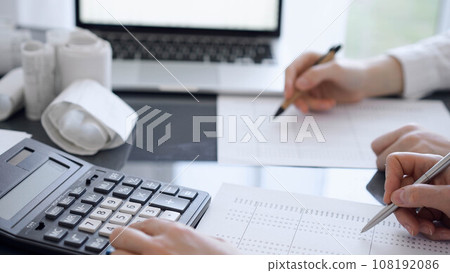 Two accountants use a calculator and laptop computer for counting taxes or revenue balance. Business, audit, and taxes concepts 108192086
