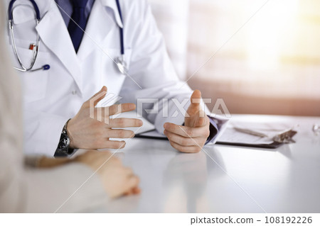 Unknown male doctor and patient woman discussing something while sittingin a darkened clinic, glare of light on the background. Close-up of hands 108192226