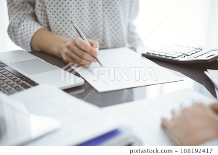 Woman accountant using a calculator and laptop computer while counting taxes for a client. Business audit concepts 108192417