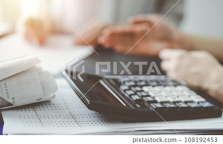 Woman accountant using a pen and laptop computer while counting and discussing taxes with a client, focus on the calculator. Business audit and finance concepts Woman accountant using a pen and laptop computer while counting and discussing taxes with a client, focus on the calculator. Business audit and finance concepts 108192453