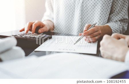 Woman accountant using a calculator and laptop computer while counting taxes for a client. Business audit and finance concepts 108192455