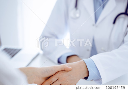 Doctor and patient shaking hands while sitting opposite of each other at the table in clinic, just hands close up. Medicine concept Doctor and patient shaking hands while sitting opposite of each other at the table in clinic, just hands close up. Medicine concept 108192459