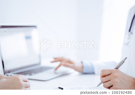 Doctor and patient discussing something and using laptop while sitting opposite each other at the desk in clinic office. Perfect medical service and medicine concept 108192480