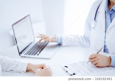 Doctor and patient discussing something and using laptop while sitting opposite each other at the desk in clinic office. Perfect medical service and medicine concept 108192481