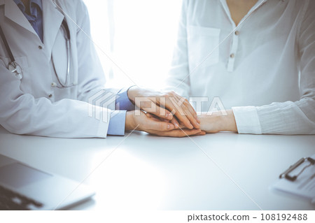 Doctor and patient sitting near each other at the table in clinic office. The focus is on female physician's hands reassuring woman, only hands, close up. Medicine concept Doctor and patient sitting near each other at the table in clinic office. The focus is on female physician's hands reassuring woman, only hands, close up. Medicine concept 108192488
