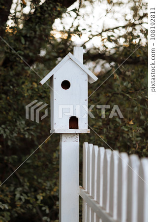 White birdhouse on white fence White birdhouse on white fence 108192811