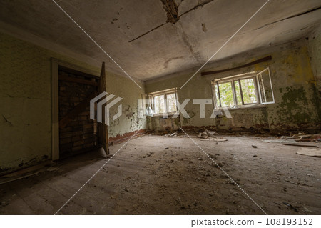 Interior of shabby abandoned house hall with rubbish dirty uncleaned marble floor broken windows door and walls with scratches cracked ceiling in daylight against blurred green trees 108193152