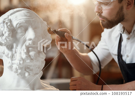 Male sculptor repairing gypsum sculpture of woman's head at the working place in the creative artistic studio. 108193517