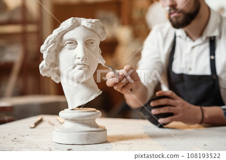 Skillful sculptor makes professional restauration of gypsum sculpture of woman's head at the creative workshop. Skillful sculptor makes professional restauration of gypsum sculpture of woman's head at the creative workshop. 108193522
