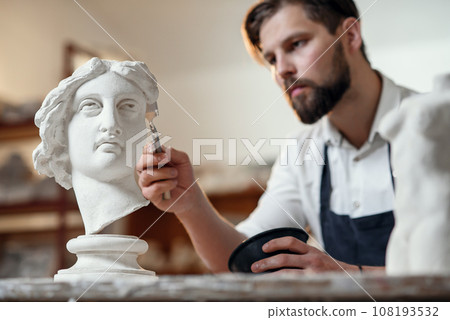 Skillful sculptor makes professional restauration of gypsum sculpture of woman's head at the creative workshop. 108193532