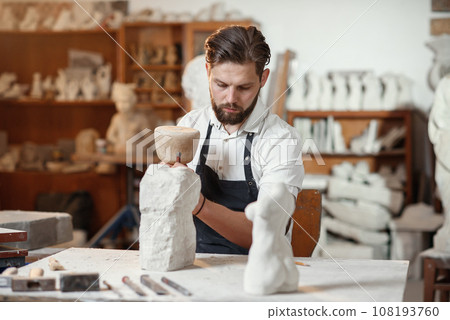 Stone carver works with wooden hammer and chisel at limestone. 108193760