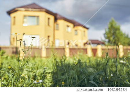 A country house with a summer garden behind a fence. The house stands in the rays of the setting sun. The concept of suburban life with space to copy. High quality photo 108194284