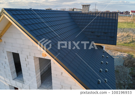 Aerial view of unfinished house with aerated lightweight concrete walls and wooden roof frame covered with metallic tiles under construction. Aerial view of unfinished house with aerated lightweight concrete walls and wooden roof frame covered with metallic tiles under construction. 108196933