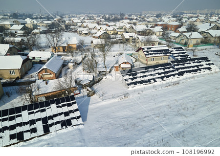 Aerial view of snow melting from covered solar photovoltaic panels installed on house rooftop for producing clean electrical energy. Low effectivity of renewable electricity in nothern region winter Aerial view of snow melting from covered solar photovoltaic panels installed on house rooftop for producing clean electrical energy. Low effectivity of renewable electricity in nothern region winter 108196992
